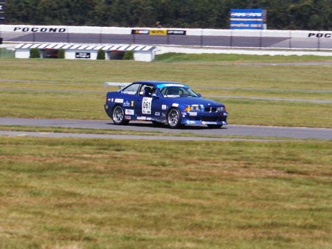 2001 Mercury Grand Marquis - A blue race car with the number 061 and sponsor decals navigates a turn on a race track.