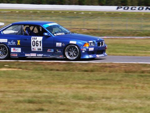 2001 Mercury Grand Marquis - A blue BMW race car speeds around a track, displaying various sponsor decals and the number 061.