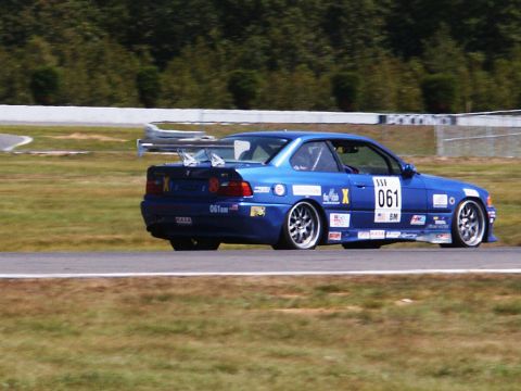 2001 Mercury Grand Marquis - A blue race car with sponsor decals and a prominent rear spoiler navigates a track.
