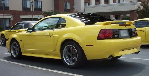 2002 Ford Mustang - A yellow Ford Mustang GT is parked in a lot, with another yellow vehicle visible beside it.