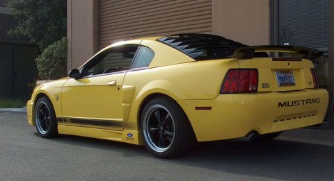 2002 Ford Mustang - A yellow 2002 Ford Mustang coupe is parked outside a building with its rear visible.
