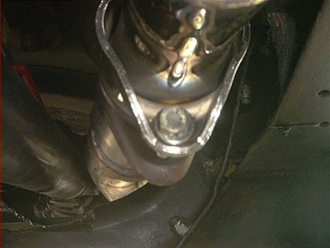 1978 Ford Bronco - Underhood close-up of a stainless exhaust pipe hand-formed with a welded seam and a deep dimple to clear a large bolt head, tucked beside a…