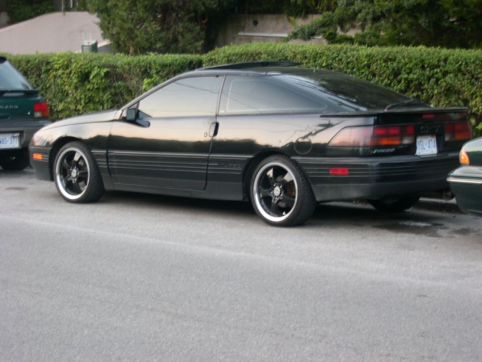 Black Ford Probe coupe on aftermarket black wheels, rear three-quarter view