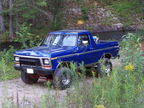 1979 Ford Bronco - This lifted blue Ford Bronco is parked off-road with vegetation surrounding it.