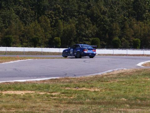 2001 Mercury Grand Marquis - A blue race car with a prominent spoiler navigates a turn on a race track.