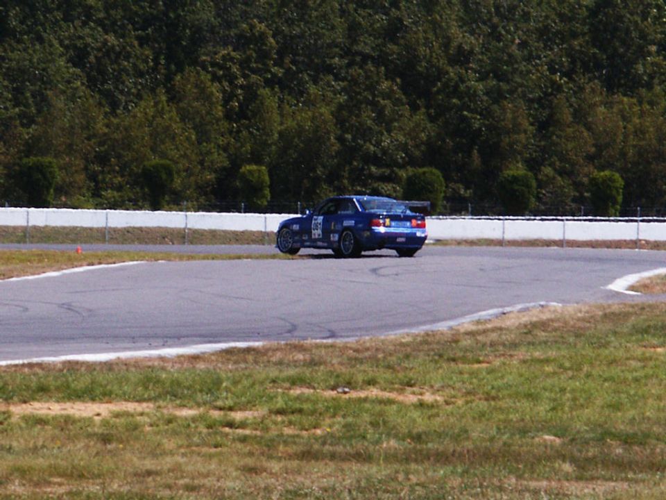 Blue race car with spoiler on track, rear view