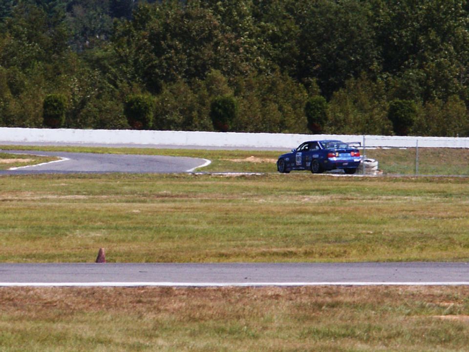 Blue sedan with a spoiler and racing decals on a track, seen from the rear