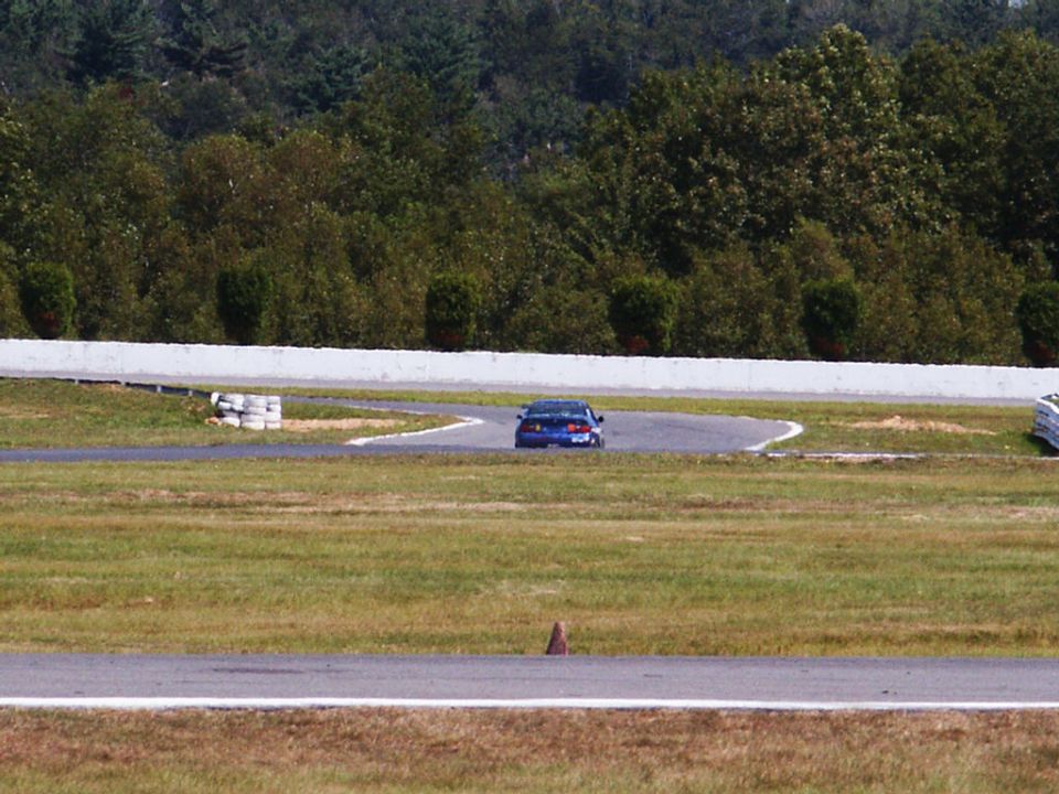 Blue sedan driving on a race track with trees in the background