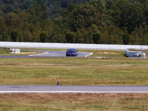 2001 Mercury Grand Marquis - A blue sedan navigates a turn on a paved race track with grassy areas and trees surrounding it.