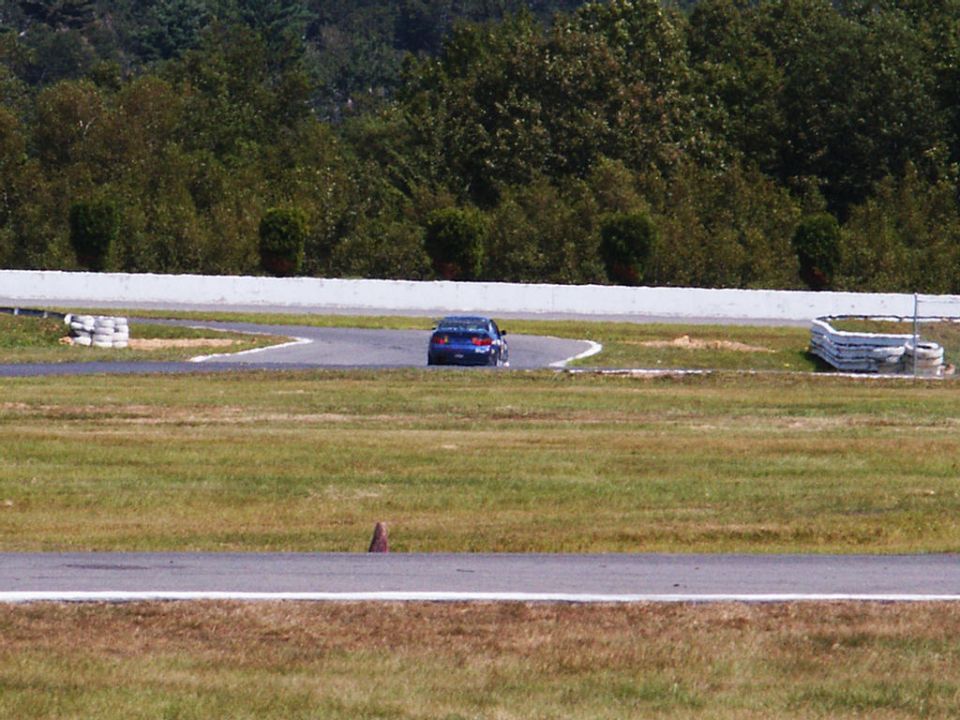 blue sedan driving on a race track, trees in background