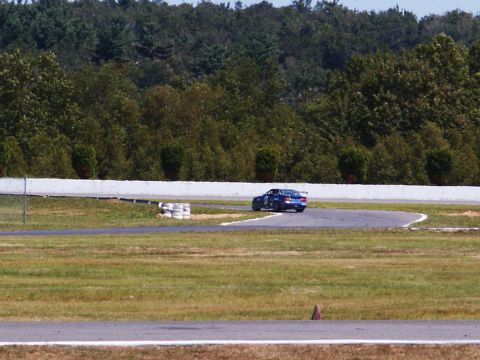 2001 Mercury Grand Marquis - A blue race car navigates a turn on a sunny day at the track, with a SUPERMOTORS watermark visible.