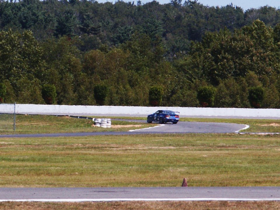 Blue race car on track, rear view. Watermark: SUPERMOTORS