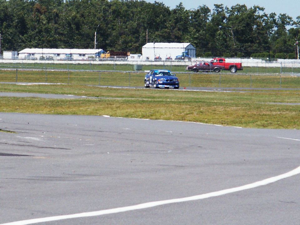 Blue race car on a track with a red pickup truck in the background