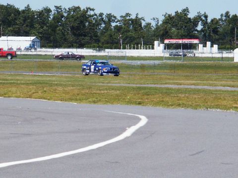2001 Mercury Grand Marquis - A blue race car navigates the track at Pocono Raceway, with other vehicles visible in the distance.
