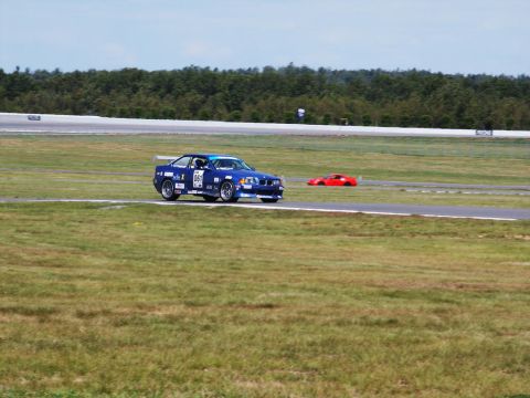 2001 Mercury Grand Marquis - A blue BMW race car navigates a turn on a sunny day at the track, with another car visible in the distance.