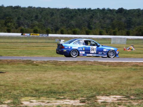 2001 Mercury Grand Marquis - A blue coupe with racing decals and a spoiler speeds around a track on a sunny day.