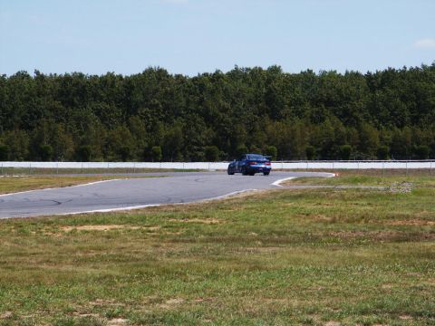 2001 Mercury Grand Marquis - A blue sedan navigates a turn on a race track, with a dense line of trees bordering the course.
