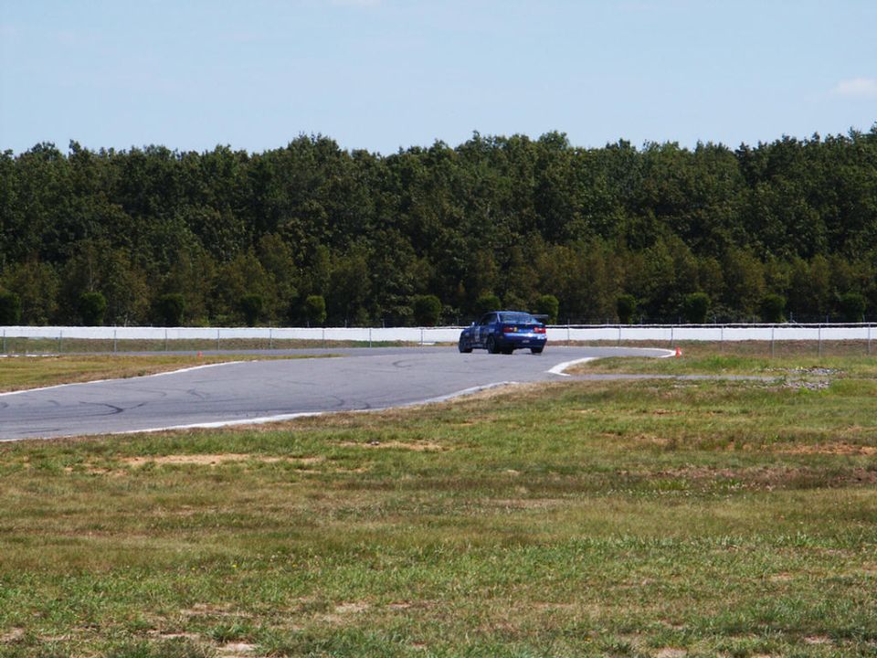Blue sedan on a race track corner, trees and sky in background