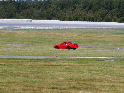2001 Mercury Grand Marquis - A red sports car is seen on a grassy area next to a race track.