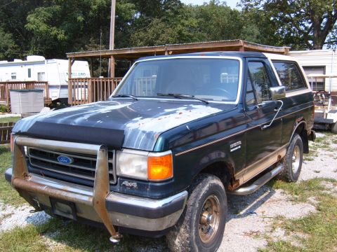 1993 Ford Bronco - This 1993 Ford Bronco is seen from a 3q-front angle, a dark green exterior with a tan stripe and a prominent brush guard.