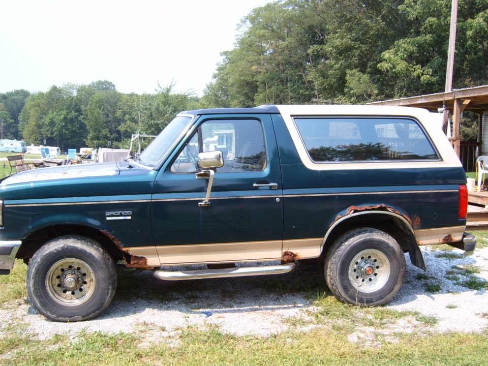 1993 Ford Bronco side view, dark green with tan trim, showing rust on wheel wells