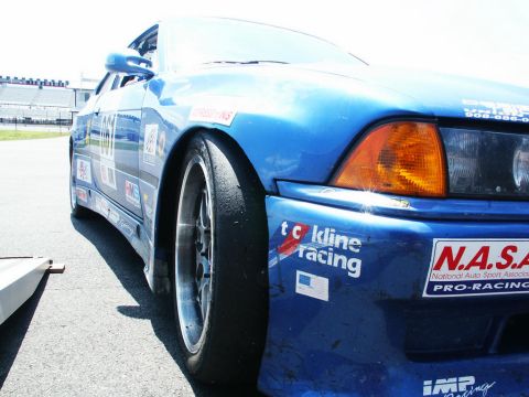 2001 Mercury Grand Marquis - A blue race car with various sponsor decals is parked on an asphalt surface, possibly a racetrack.