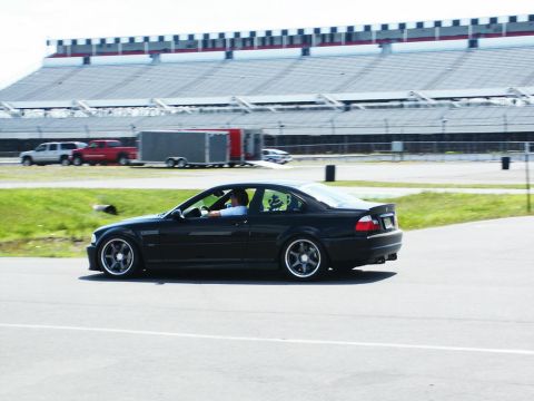 2001 Mercury Grand Marquis - A black coupe drives on a track with grandstands in the background. Other vehicles and a trailer are also present.