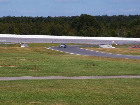 2001 Mercury Grand Marquis - A silver sports car navigates a turn on a race track, with another vehicle visible in the distance.