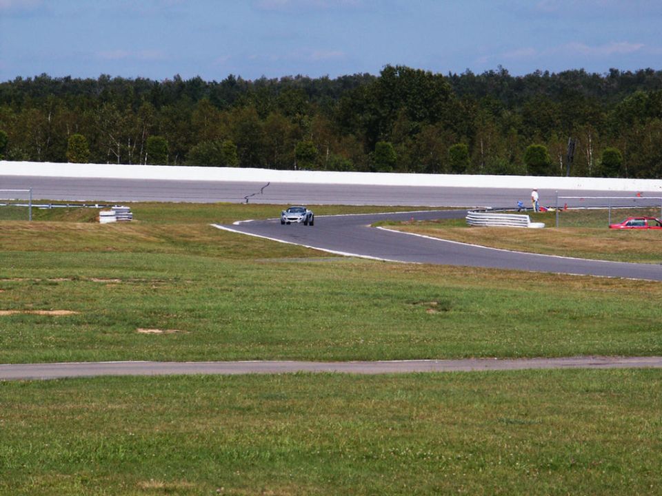 Silver sports car on a race track with a red car parked in the background