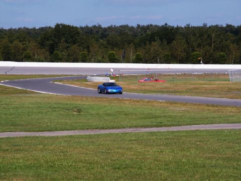 2001 Mercury Grand Marquis - A blue sports car navigates a turn on a race track, with another vehicle visible in the distance.