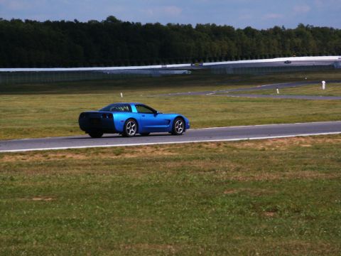 2001 Mercury Grand Marquis - A blue sports car drives on a race track with grassy areas and trees in the background.