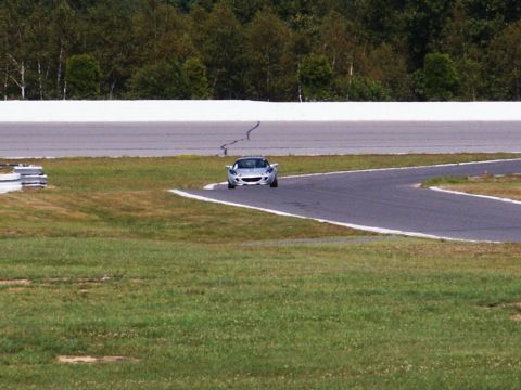 2001 Mercury Grand Marquis - A silver sports car navigates a turn on a race track with trees in the background.
