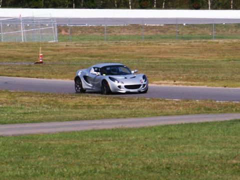 2001 Mercury Grand Marquis - A silver Lotus Elise is seen on a race track, with green grass and a fence in the background.