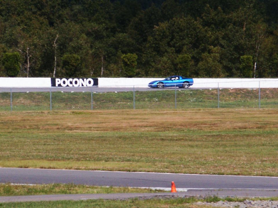 Blue sports car on a race track, side view. Pocono sign visible