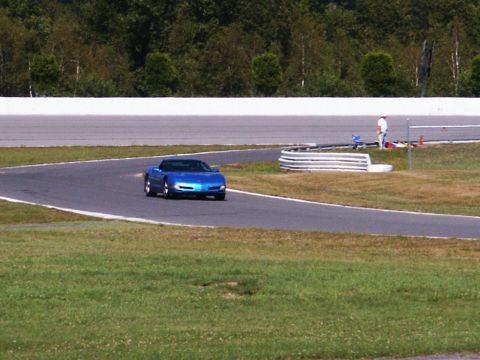 2001 Mercury Grand Marquis - A blue convertible sports car navigates a turn on a race track with a person standing trackside.