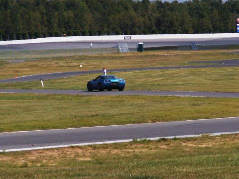 2001 Mercury Grand Marquis - A blue sports car is on a race track with trees and a white barrier in the background.