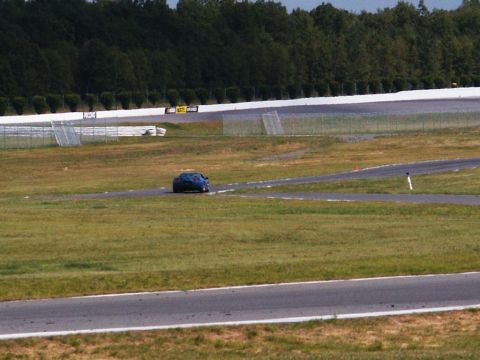 2001 Mercury Grand Marquis - A blue sports car navigates a turn on a race track, with trees and fencing in the background.