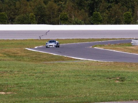 2001 Mercury Grand Marquis - A silver sports car navigates a turn on a paved race track with grassy verges.