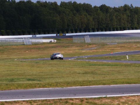 2001 Mercury Grand Marquis - A silver sports car drives on a race track with trees and fencing visible in the background.