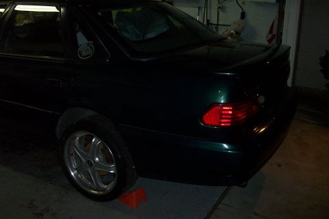 1995 Ford Taurus - The rear of a dark green sedan is shown, with a spoiler and custom wheels visible. The vehicle is parked indoors.