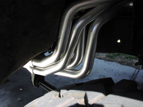 1979 Ford Bronco - Chrome exhaust headers are visible under the frame of a vehicle, near a tire.