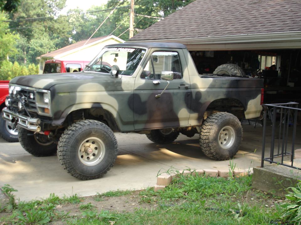 Camouflage-painted lifted Ford Bronco with big mud tires parked in driveway