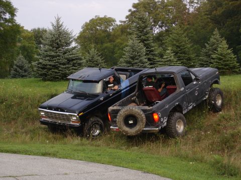 1979 Ford Bronco - Two Ford Broncos are parked on a grassy incline, surrounded by trees and foliage.