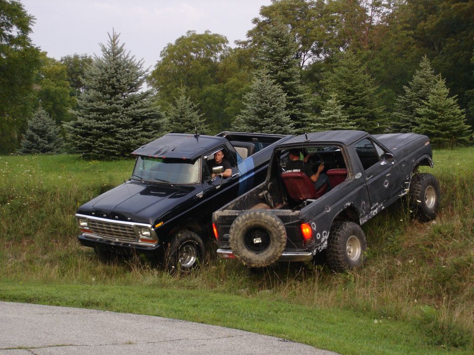 Two black Ford Broncos parked on a grassy hill. One has a blue stripe on its side