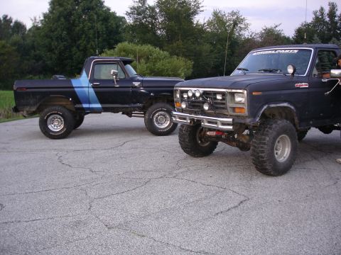1979 Ford Bronco - Two lifted 1979 Ford trucks, a pickup and a Bronco, are parked on asphalt with trees in the background.