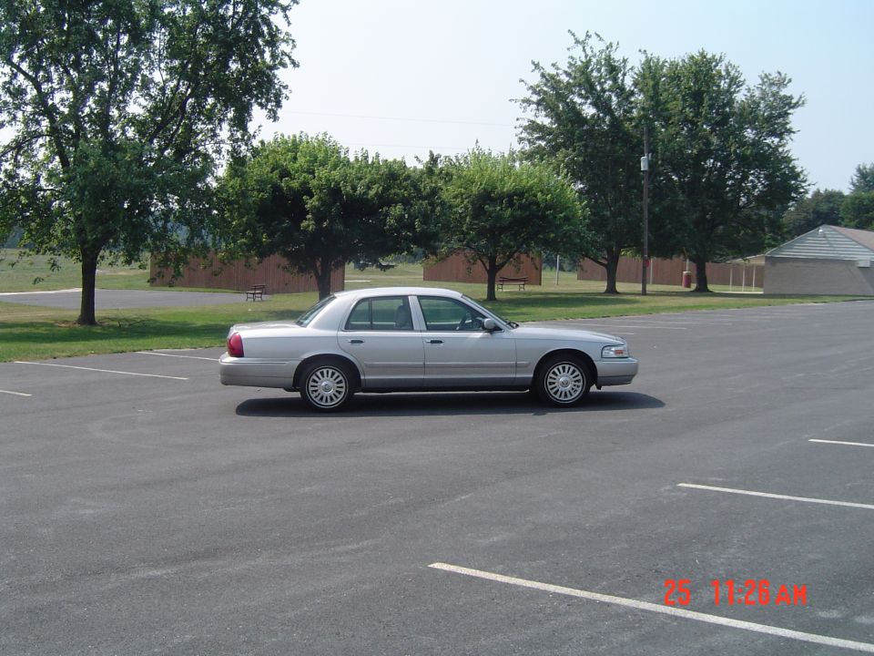 Silver sedan parked in a lot with trees and a building in the background