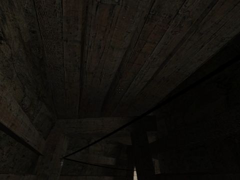1969 Ford Mustang - A dimly lit scene reveals the rough texture of a wooden interior, possibly a barn or shed, with visible beams and planks.