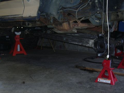 1991 Ford Bronco - The undercarriage of a vehicle is visible, supported by red jack stands, with suspension and frame components exposed.