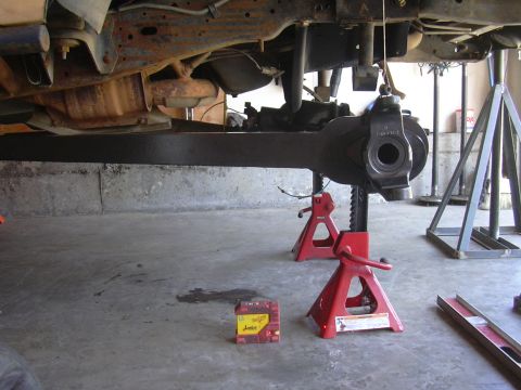 1991 Ford Bronco - Vehicle's undercarriage, including suspension components and differential, is supported by red jack stands in a garage.
