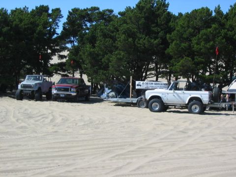 1995 Ford Bronco - A white Ford Bronco is parked on the sand with other vehicles and trees in the background.